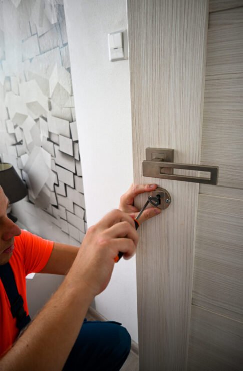 Handyman wearing an orange shirt is using a screwdriver while working on a door lock